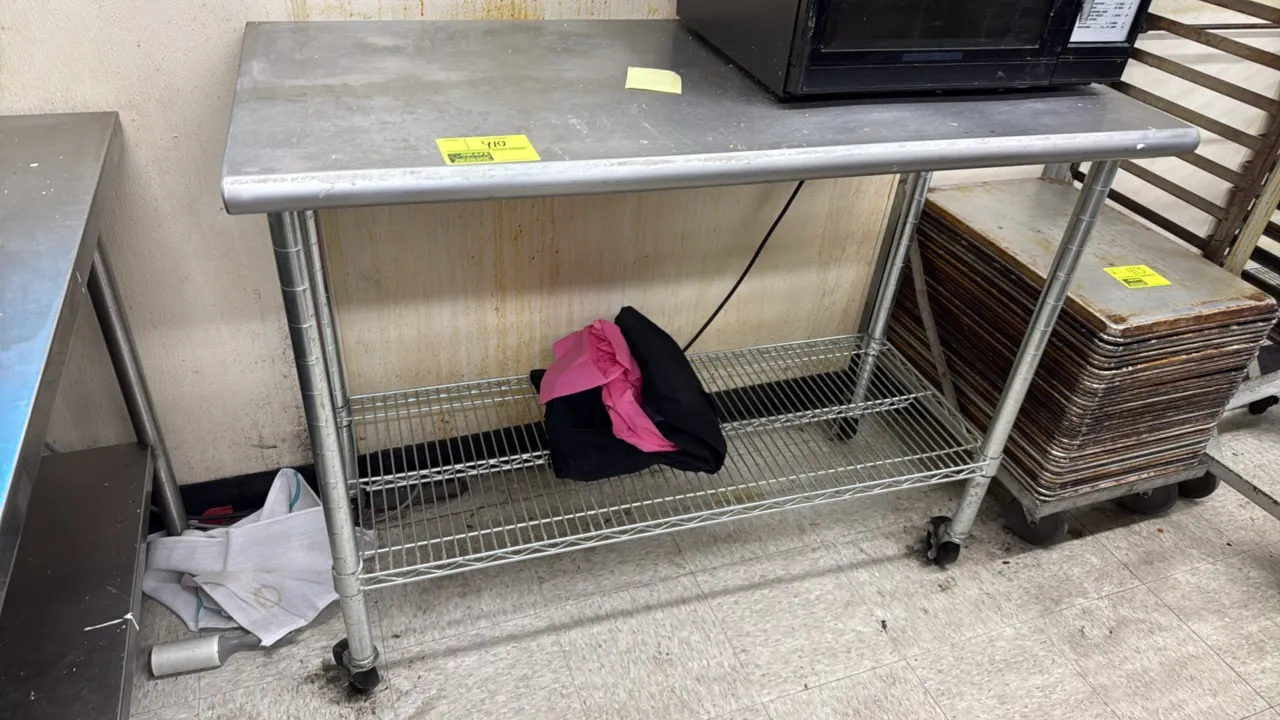Stainless steel work table. Features a bullnose front edge and wire undershelf. 50" x 24". Mounted on casters. Microwave and contents not included.
