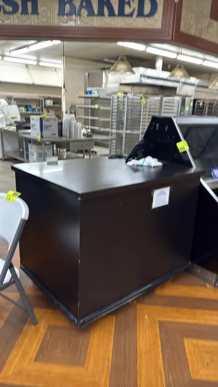 Black laminate bakery service counter. Features flat black countertop and rear open storage cavity with an adjustable shelf. 4'L. Telephone and backgr