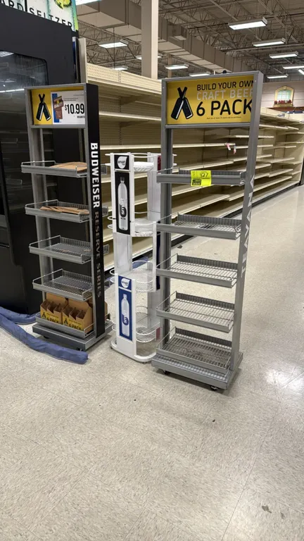 Assorted retail merchandiser display racks. Includes (2) metal mobile racks with multi-tier wire shelf baskets and top signage headers, mounted on cas