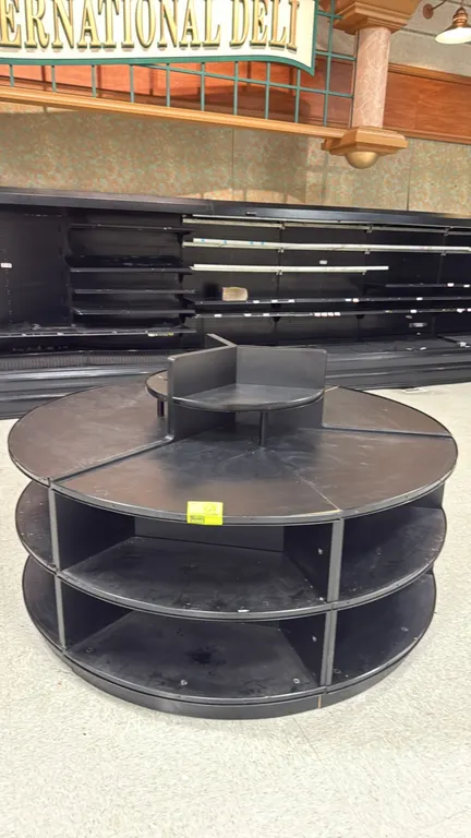 Round island merchandiser. Features black laminate construction, multi-tier perimeter display shelving, and center display riser. 6' Dia.