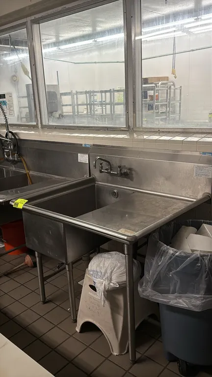 Stainless steel 1-compartment sink. Features a right drainboard, high backsplash, splash-mount faucet, and rolled rim edges. 44" x 36". Mounted on tub