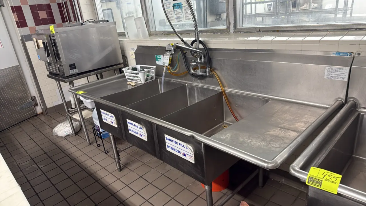 Stainless steel 3-compartment sink. Features left and right drainboards, integrated backsplash, splash-mounted faucet with pre-rinse sprayer, and chem