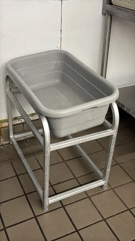 Poly meat lug with aluminum stand. Features a gray polyethylene lug tub and a welded tubular aluminum frame stand.