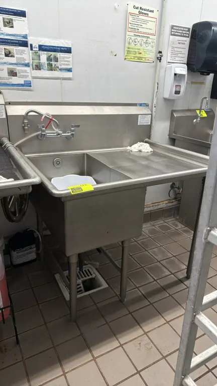 Stainless steel 1-compartment sink with right drainboard. Features integrated backsplash, splash-mount faucet with swing spout, rolled rim edges, and