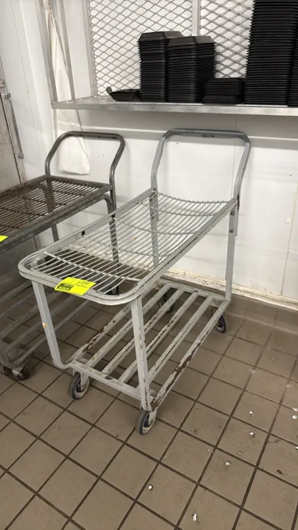 Metal 2-tier warehouse cart. Features an upper wire shelf, lower slatted shelf, and integrated push handle. 36"L. Mounted on casters.