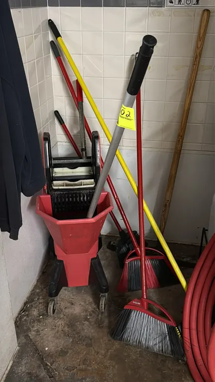 Janitorial cleaning lot. Includes mobile mop bucket with wringer, assorted angle brooms, and utility handles. Mop bucket mounted on swivel casters. Ba
