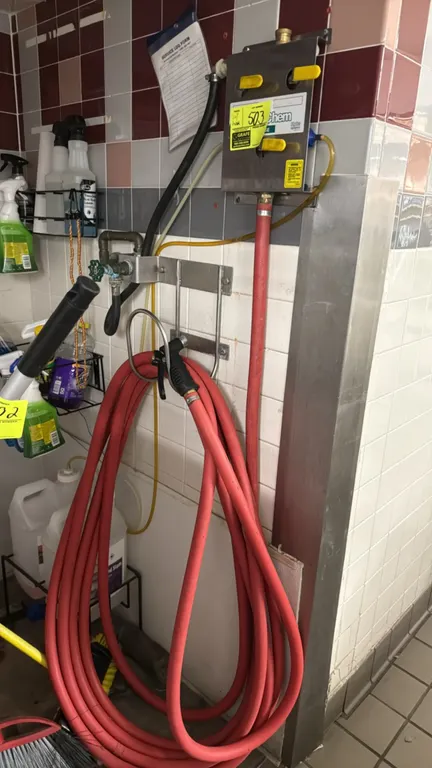 Hydro Systems wall-mounted chemical dispenser. Features stainless steel housing with 3 selector valves, red washdown hose with spray nozzle, and wall-