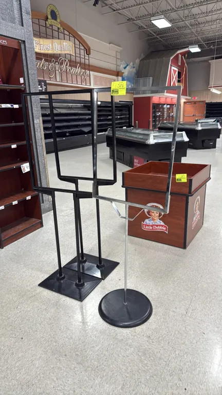 Assorted metal retail floor sign stands. Includes (2) black metal dual-pole stands with rectangular bases and (1) chrome single-pole stand with round