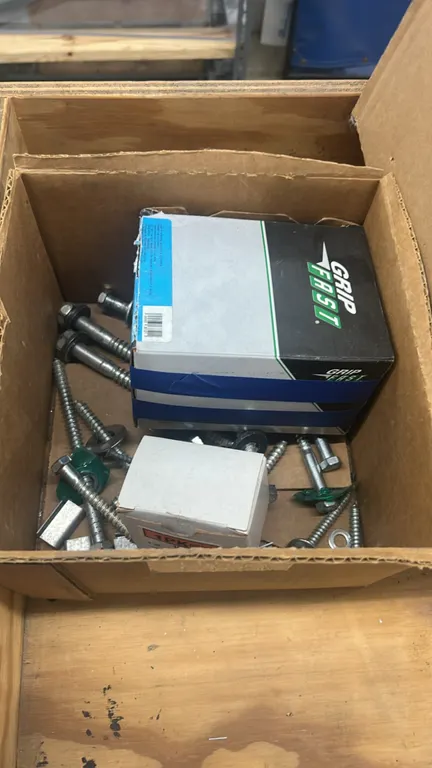 Assorted hardware and fasteners. Includes lag bolts, screws, washers, brackets, metal strapping seals, Grip Fast fasteners, and remaining boxed conten