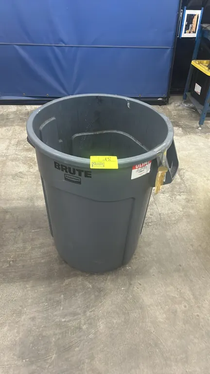 Rubbermaid Brute polyethylene trash bin. Features integrated side handles and molded venting channels. Gray plastic construction. Contents not include