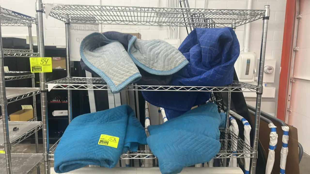 Quilted moving blankets. Features assorted sizes, blue color tones, and stitched construction. Wire shelving and background items not included.