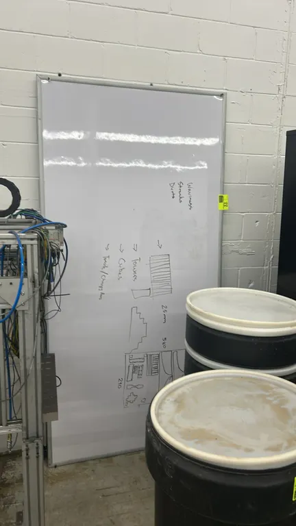 Aluminum framed whiteboard. Features a white dry erase surface and aluminum perimeter frame. Dimensions: 8' x 4'. Surrounding equipment and barrels no