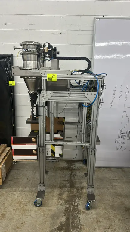 Semi-automatic dual-head powder auger filler and dosing machine. Features dual stainless steel hoppers, push-button operator control stations, and cab