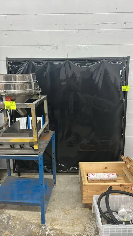 Metal framed divider screen. Features a dark tinted flexible vinyl curtain secured with grommets to a rectangular metal frame. Dimensions: 72" x 74".