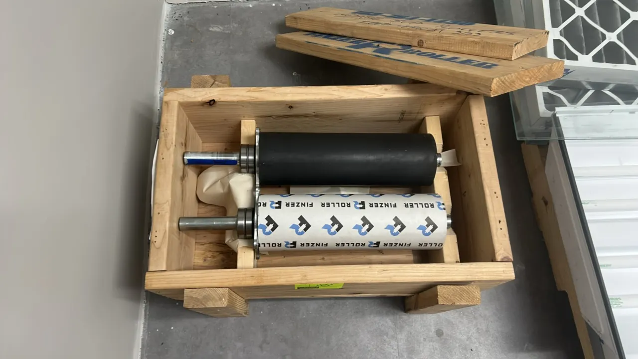 Finzer industrial replacement rollers. Includes (2) rubber-coated rollers with extended steel shafts, mounted bearings, and flanges. Housed in a fitte