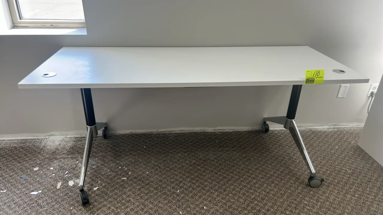 Laminate mobile collapsible table. Features a white laminate top with dual wire management grommets. 71"L x 28"W. Mounted on a metal base with casters