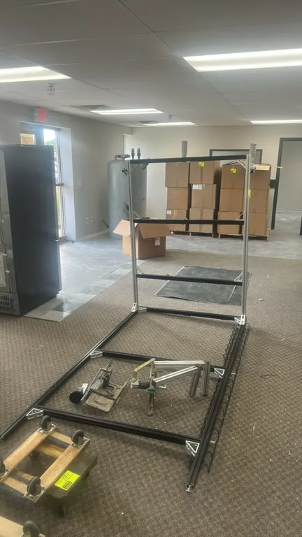 Modular extruded metal frame structure. Features T-slot framing construction, corner gussets, attached wire wireway tray, and assorted loose bracket h