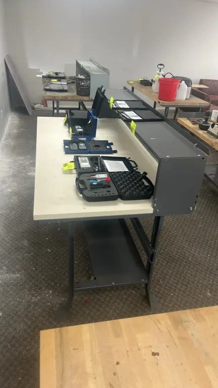 Laminate top workbench. Features a metal frame, upper riser shelf, and lower storage shelf. 6' x 3'. Contents not included.