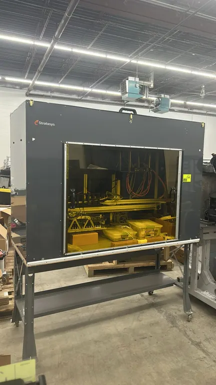 Stratasys FDM 3D printer. Features an enclosed build chamber with yellow-tinted sliding front viewing doors, internal gantry system, and cable managem