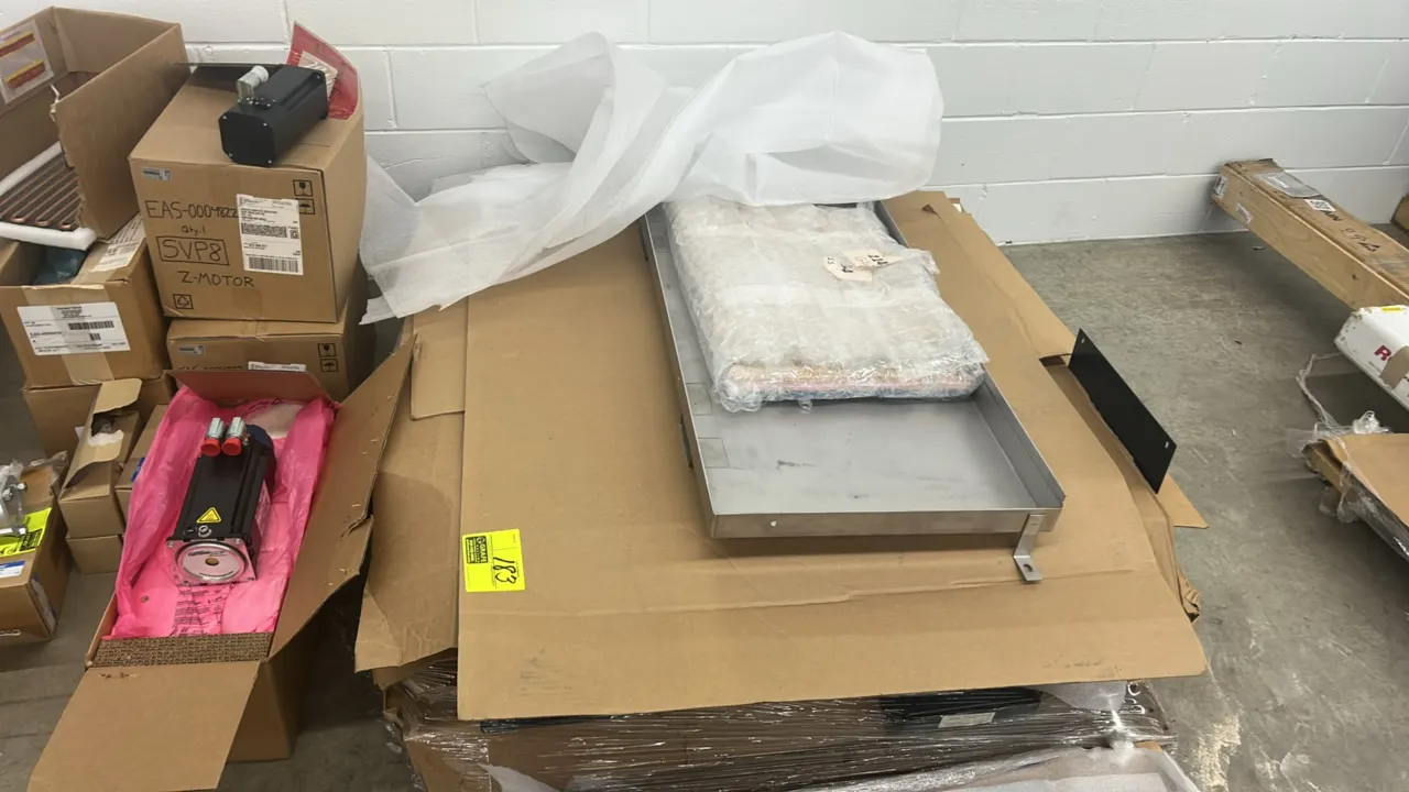 Assorted metal frames and components. Includes stainless steel and painted metal frames, trays, and related parts packaged on a pallet with protective