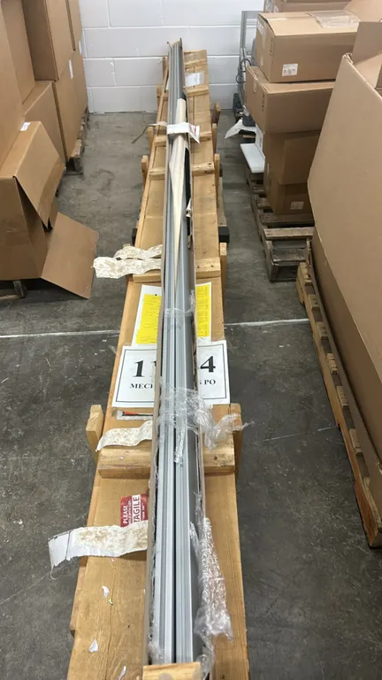 Assorted metal mechanical and electrical components. Includes long metal extrusions, channel tracks, and boxed hardware stored in a wooden shipping cr