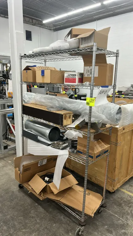Metal multi-tier portable wire shelving rack with contents. Includes HVAC components, ductwork, assorted electrical cords, mechanical parts, and boxed