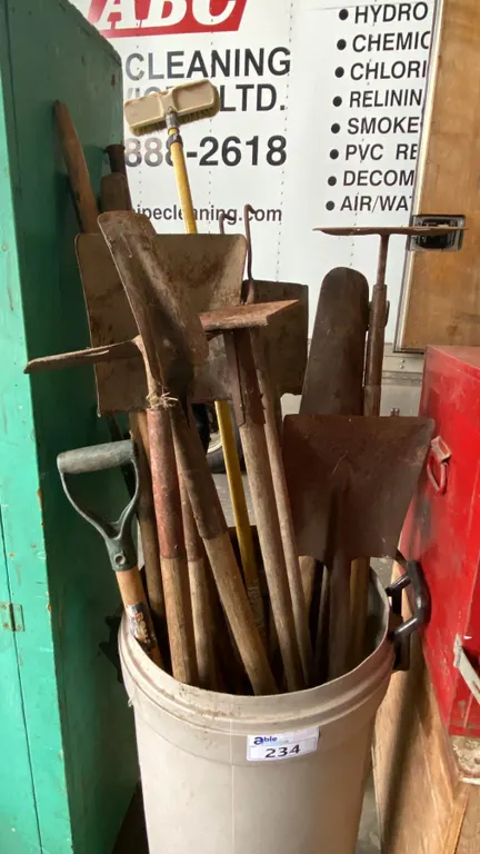BIN OF ASSORTED SHOVELS, PICK AX & 2 MANHOLE LIFTERS