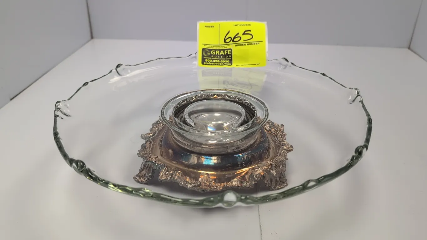 Rotating glass cake plate. Features a clear glass plate with a scalloped rim, mounted on an ornate footed metal revolving base. Dimensions: 13" Dia.