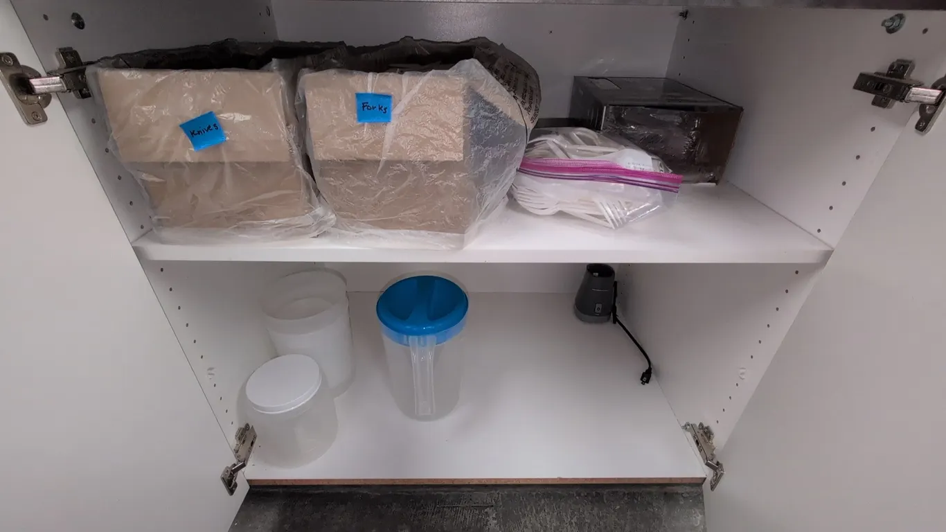 Assorted kitchen contents and dishware. Includes Hamilton Beach blender base, disposable plastic cutlery, metal flatware and prep utensils, plastic fo