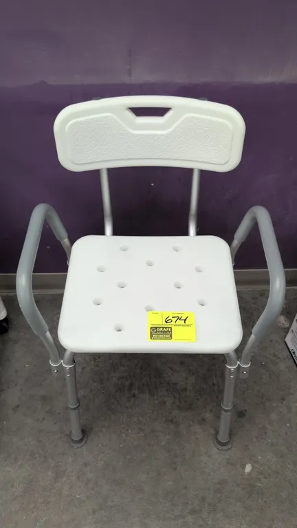 Shower chair. Features molded plastic seat with drainage holes, backrest with integrated handle cutout, padded armrests, and lightweight metal tubular