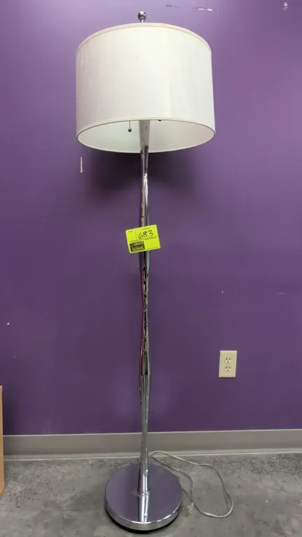 Metal floor lamp with shade. Features chrome-finish sculpted metal body, dual pull-chain sockets, and white fabric drum shade. Mounted on a round chro