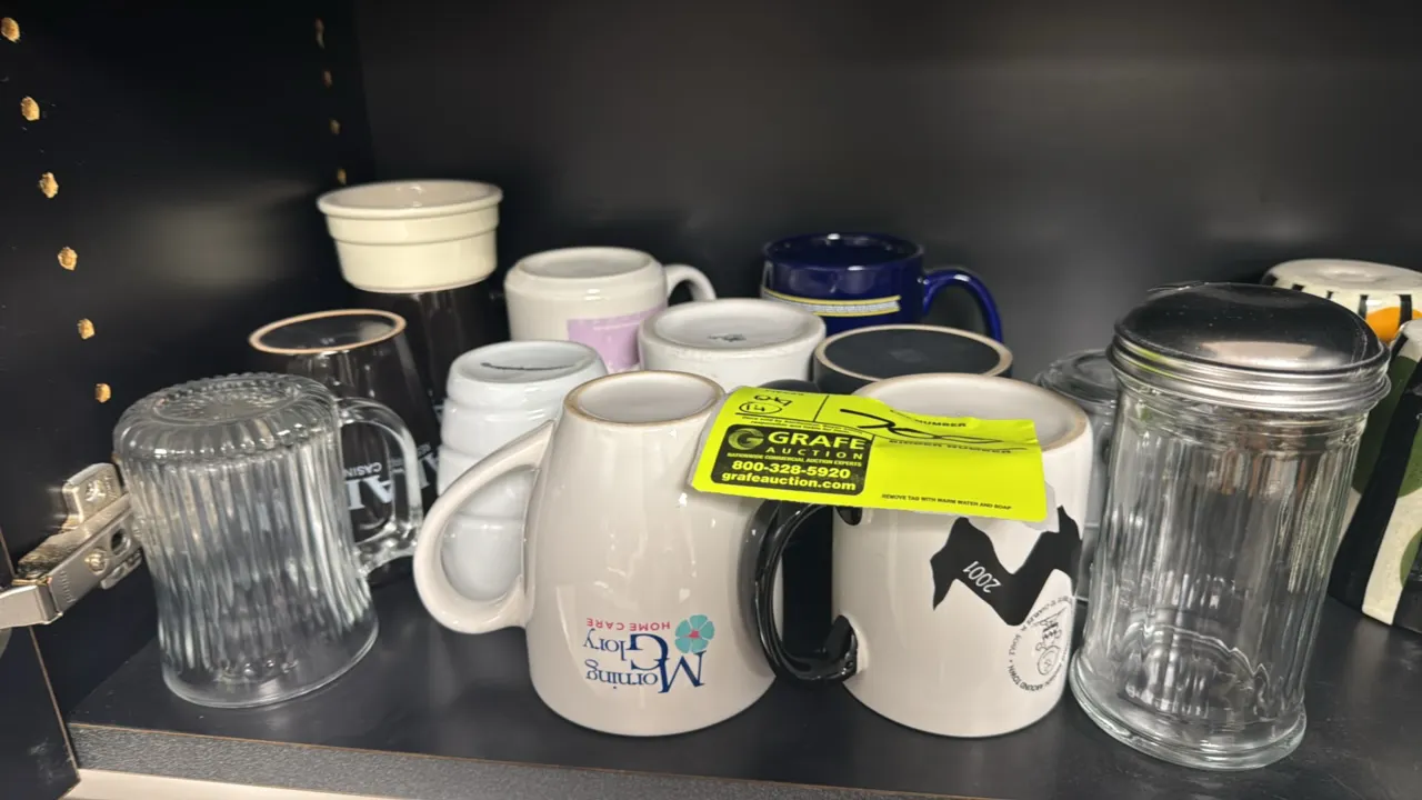 Assorted coffee cups and sugar dispenser lot. Includes various ceramic and glass coffee mugs with assorted novelty and promotional designs, accompanie