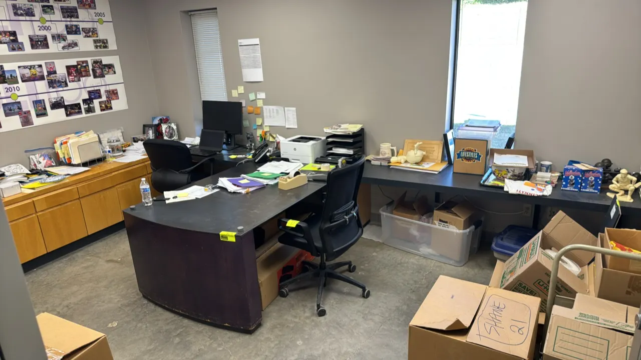 Custom L-shaped desk suite with built-in cabinets. Features laminate work surfaces and wood-finish lower storage cabinetry with doors and drawers. Dim