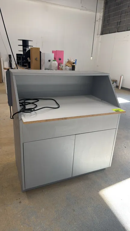 Laminate work station. Features an upper hutch enclosure, two lower cabinet doors, and a side-mounted multi-outlet power strip. Dimensions: 40" x 26".