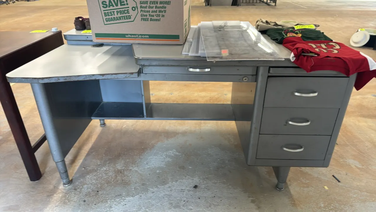 Metal desk. Features a right-hand single pedestal with three drawers, center lap drawer, pull-out reference slide, and a lowered left-hand return. 60"