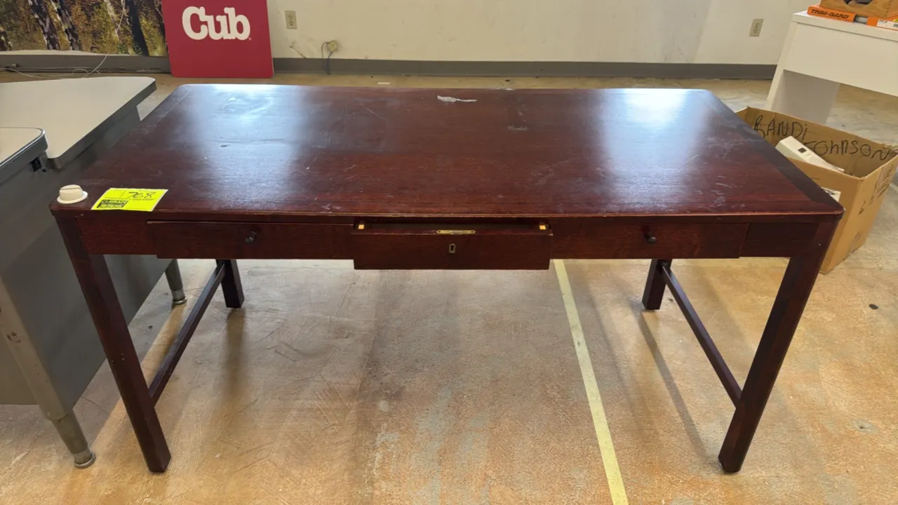 Wood 3-drawer desk. Features three front drawers with center locking drawer and side stretcher base. Dark wood finish. Dimensions: 57" x 28".