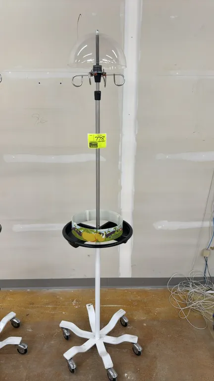 Pediatric mobile IV pole stand. Features a 4-hook top assembly beneath a clear acrylic dome, adjustable stainless steel upright, and mid-height circul