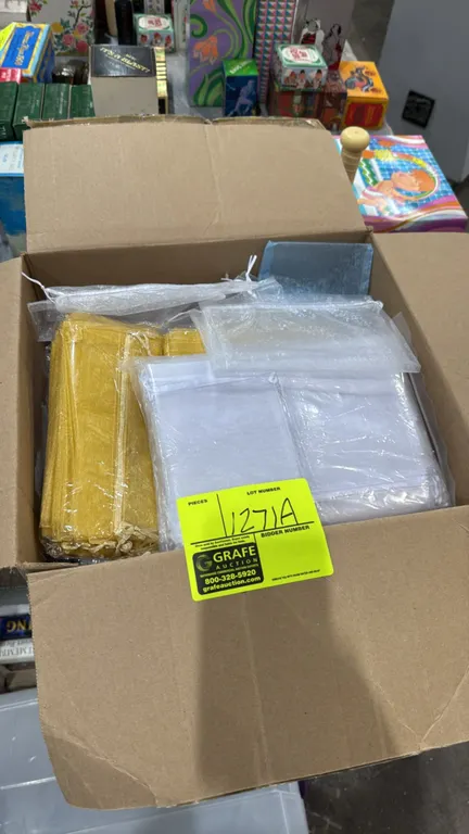 Box of assorted sheer gift bags. Features various sizes in gold and white organza fabric with drawstring closures.