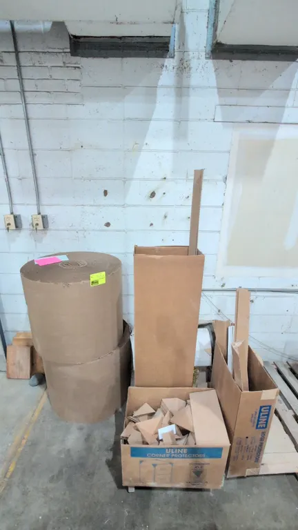 Assorted shipping and packaging materials. Includes (2) rolls of corrugated cardboard wrap, a box of Uline corner protectors, cardboard edge protector