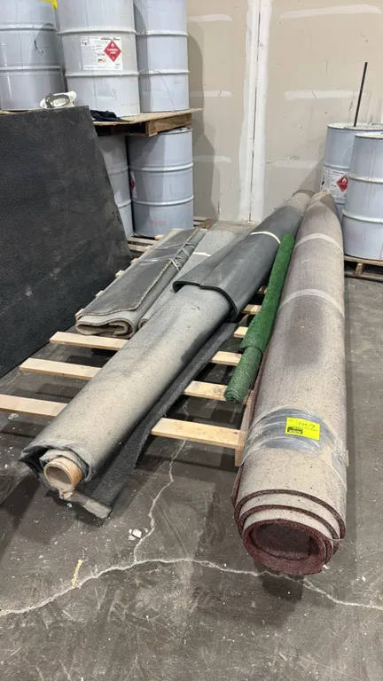 Package lot of assorted carpet and turf rolls. Includes multiple rolled and folded carpet remnants in various colors including charcoal, burgundy, and