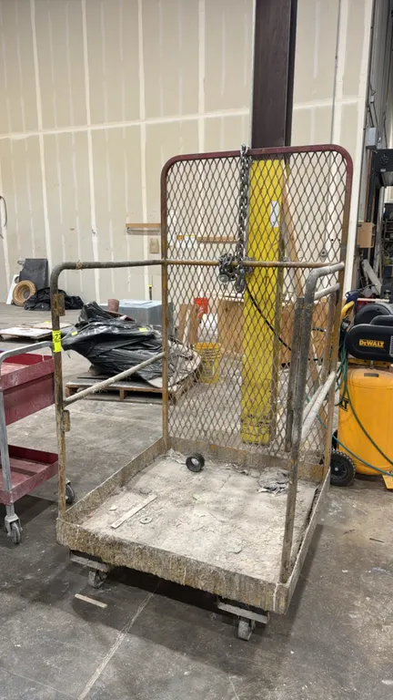 Metal portable forklift safety cage. Features expanded metal mesh back screen, tubular steel railing, safety chain with hook, and underside fork pocke