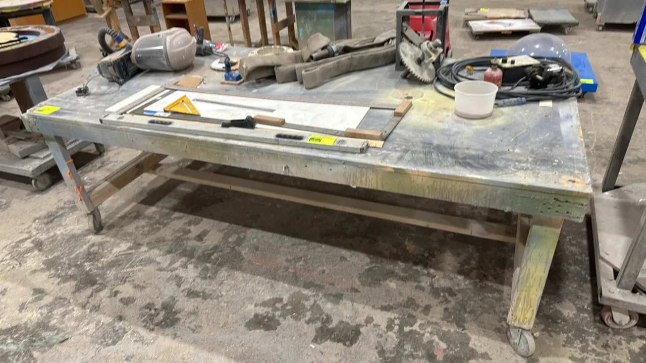 Custom wood mobile workbench. Features wood frame construction with reinforced lower stretchers. 8'L x 4'W. Mounted on swivel casters. Contents not in