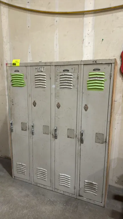 Metal 4-door locker unit. Features four compartments with upper and lower louvered ventilation, lift handles with padlock hasps, and wood side panels.
