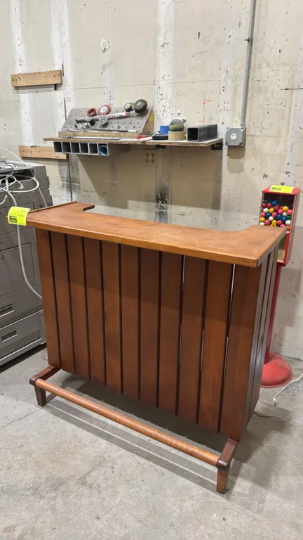 Vintage wood home bar. Features vertical slat front panel design, integrated lower wooden footrest rail, contoured countertop with raised edge trim, a