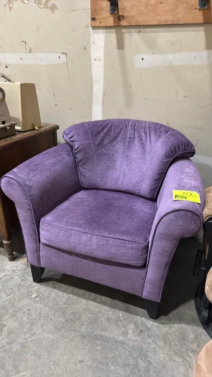 Plush armchair. Features purple textured fabric upholstery, rolled arms, padded back, and a removable seat cushion. Supported by tapered wooden legs.