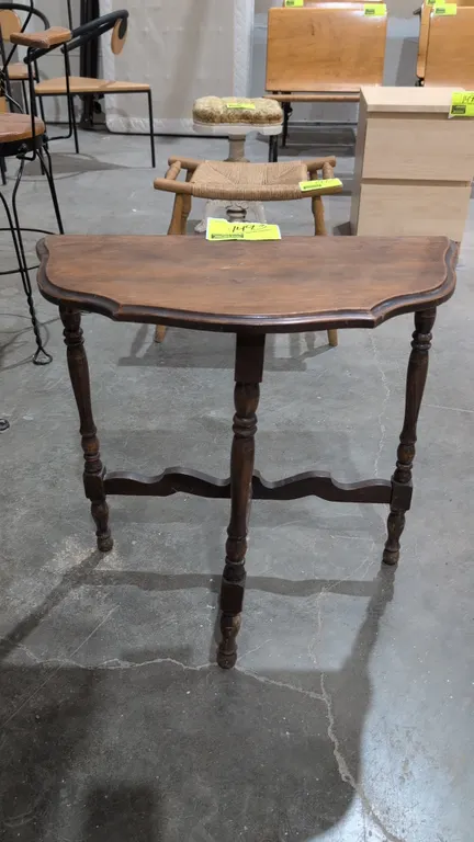 Wood demi-lune side table. Features a shaped top, three turned legs, and a decorative curved lower stretcher base. Dimensions: 24" x 24"H.