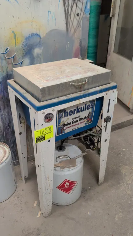 Herkules automatic paint gun washer. Features pneumatic double-diaphragm pump, solvent recovery basin, hinged lid, and steel support stand. Powered by