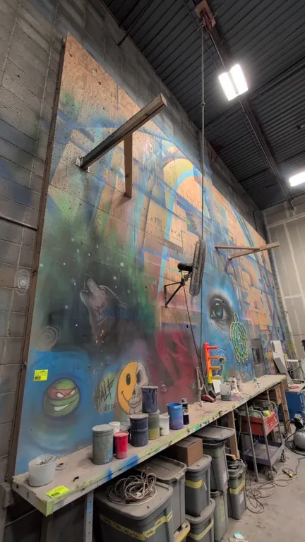 Painted plywood sheets. Features multi-color painted mural and graffiti art graphics across panels. Dimensions: 4' x 8' each. Wall-mounted fan, workbe
