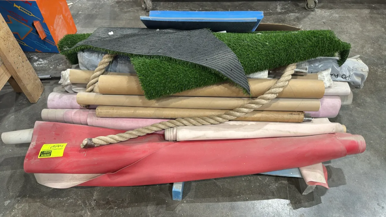 Bulk lot of various material rolls and supplies. Includes artificial turf roll and matting, assorted fabric and vinyl material rolls, a length of thic