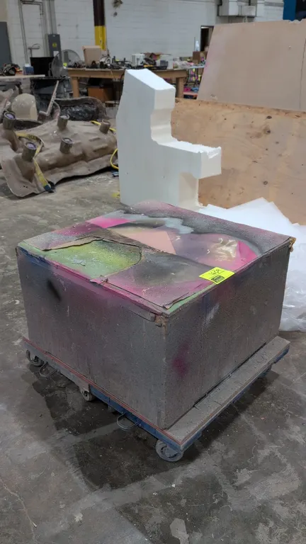 Wood portable pedestal. Constructed of wood and mounted on a mobile platform base with swivel casters. Features protective paper covering on top surfa
